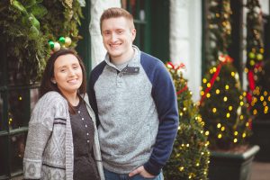 A man and woman posing for a portrait in front of a Christmas tree.