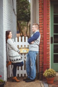 A engaged couple posing for a portrait against a white picket fence in Downtown Annapolis.