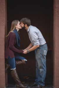 An engaged couple sharing a passionate kiss in front of a door.