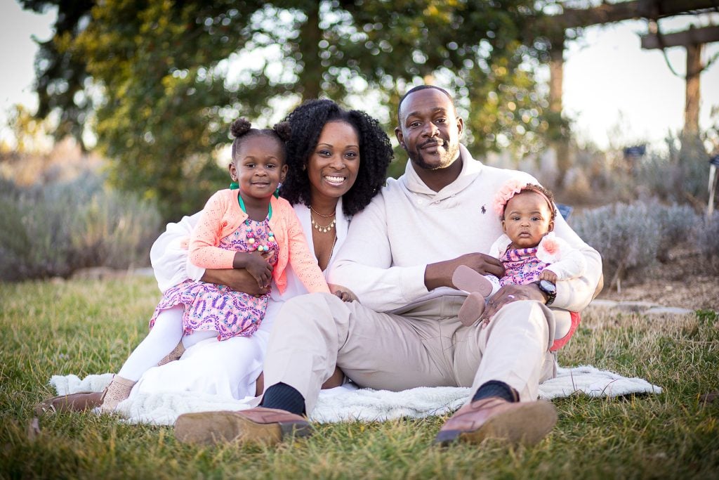 A family sitting on the grass with two small children.