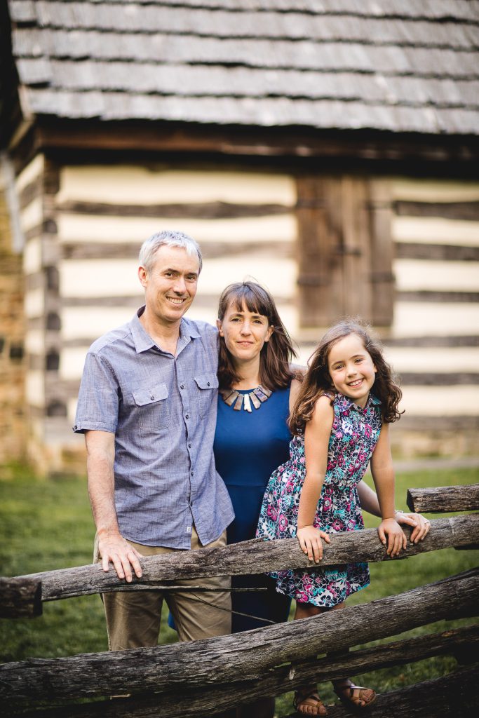 A family poses for a photo in front of a log cabin.