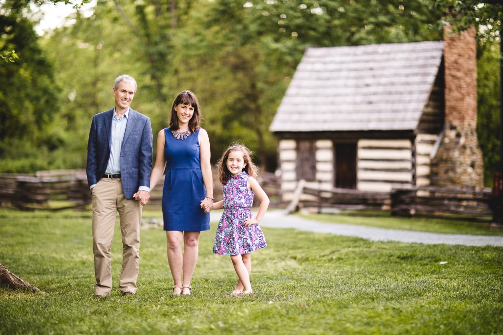 A family stands in front of a log cabin.