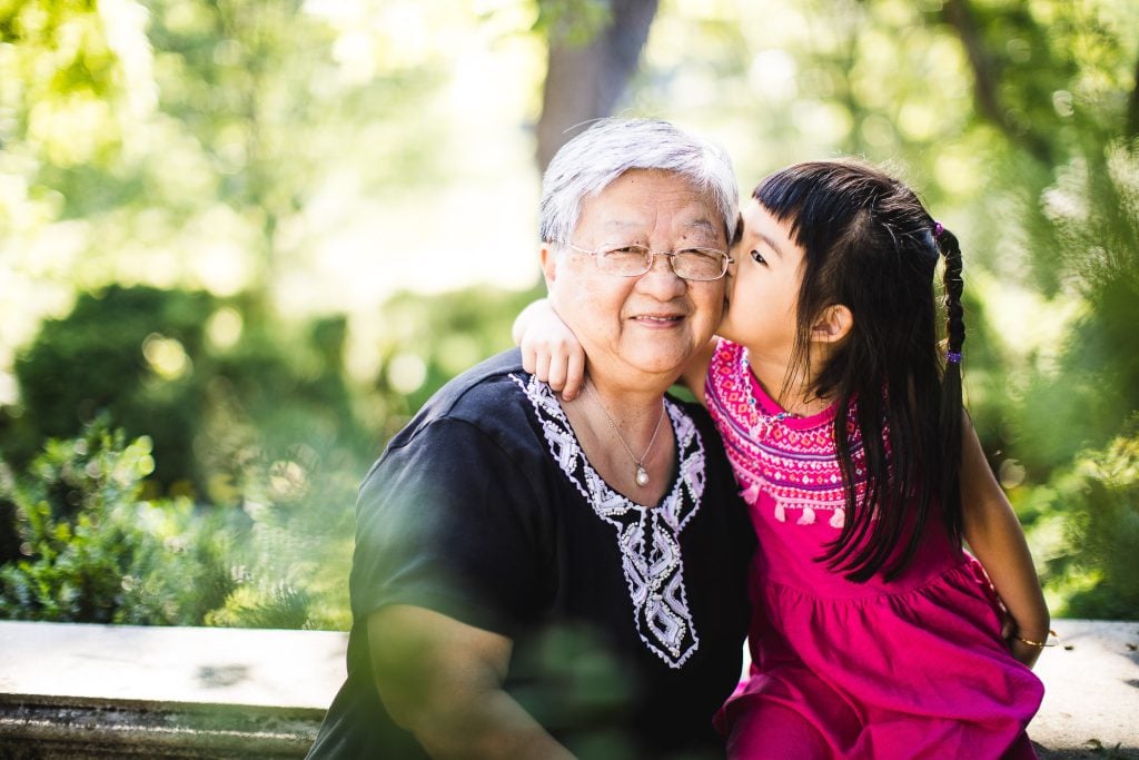 An asian grandmother kissing a little girl in the park.