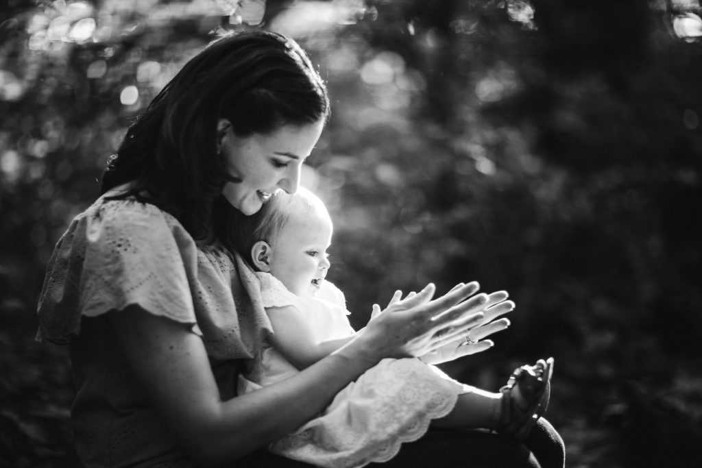 A black and white photo of a woman holding a baby in the woods.