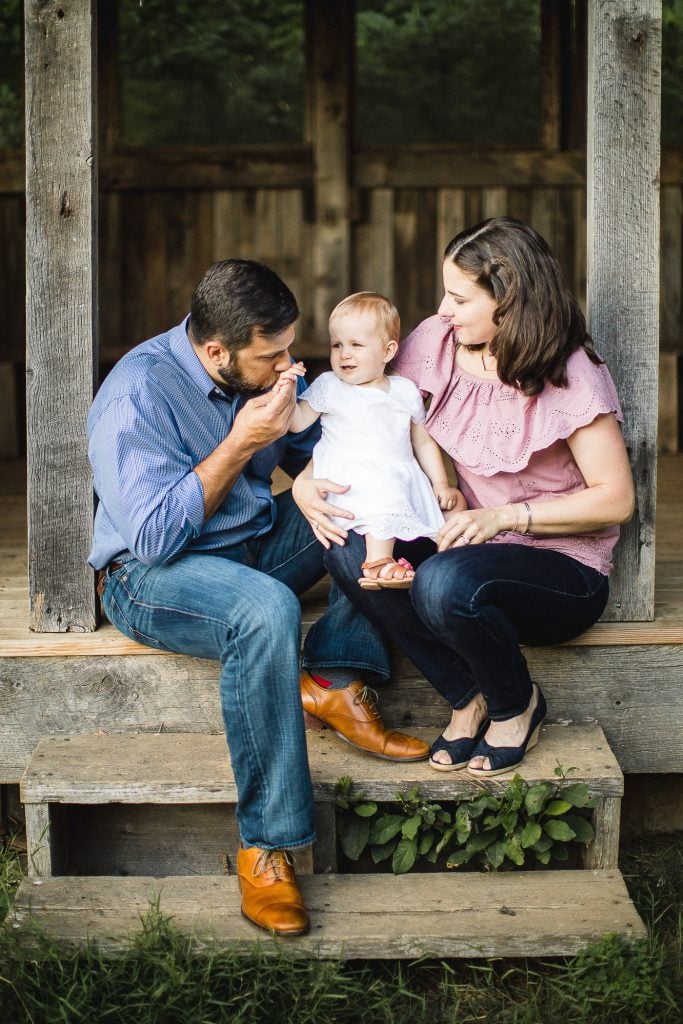 A family sits on a wooden bench with a baby in their arms.