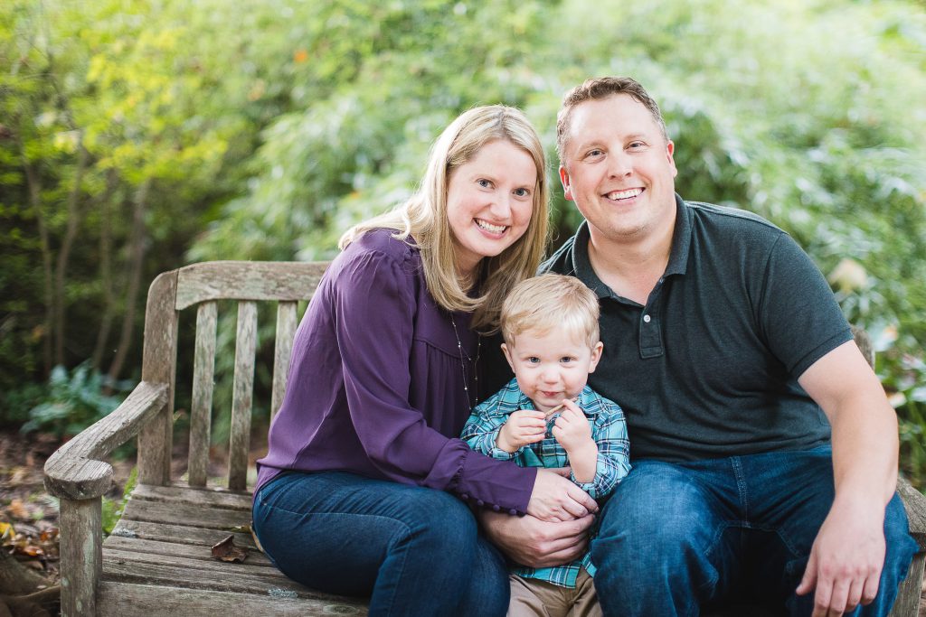 A family sits on a bench and poses for a photo.