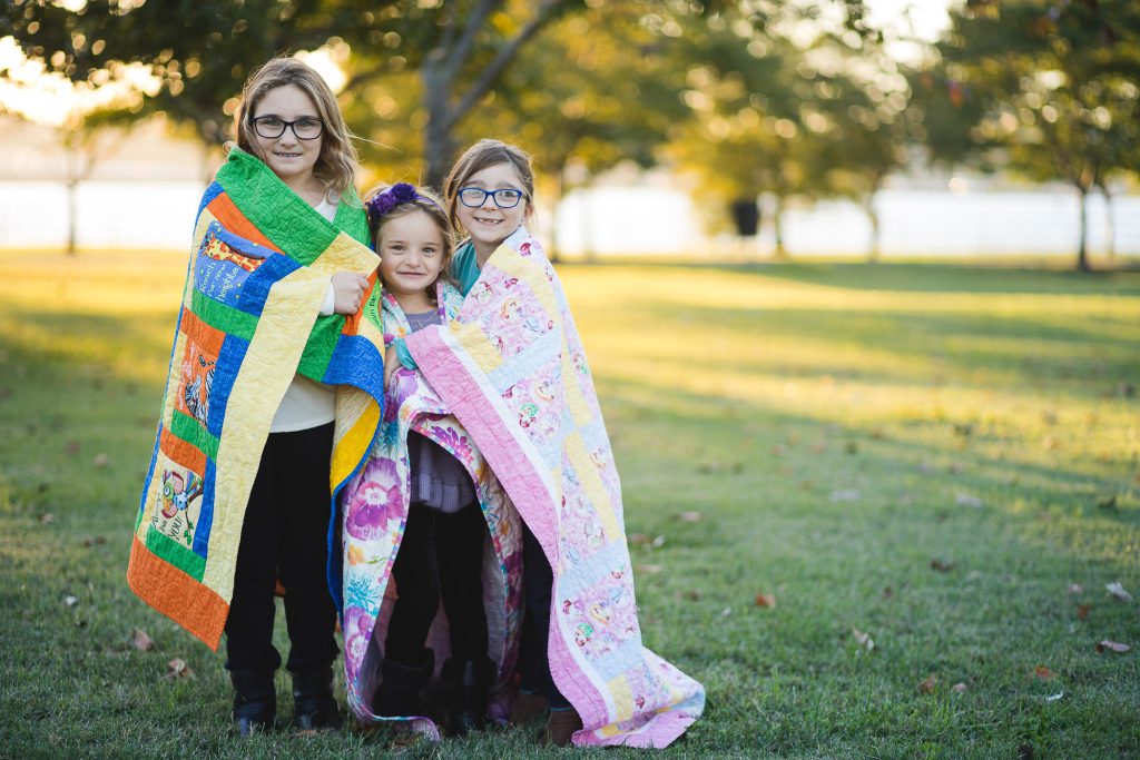Three girls standing in a field holding quilts.
