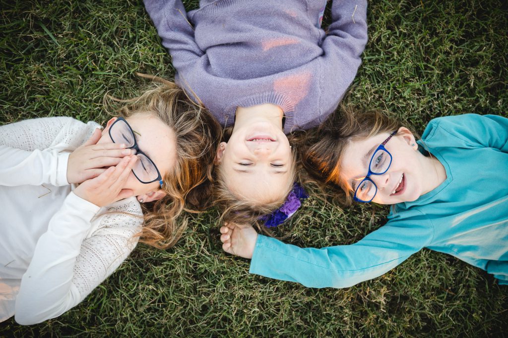 Three little girls laying on the grass laughing.