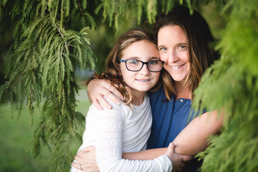 A mother and daughter hugging under a tree.