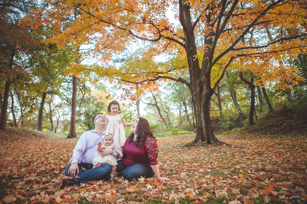 A family is posing for a fall family photo in a park.