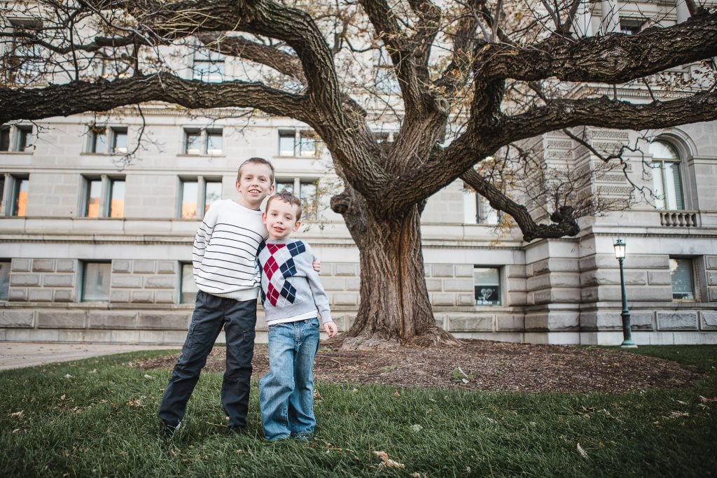 Two boys standing under a tree in front of a building.