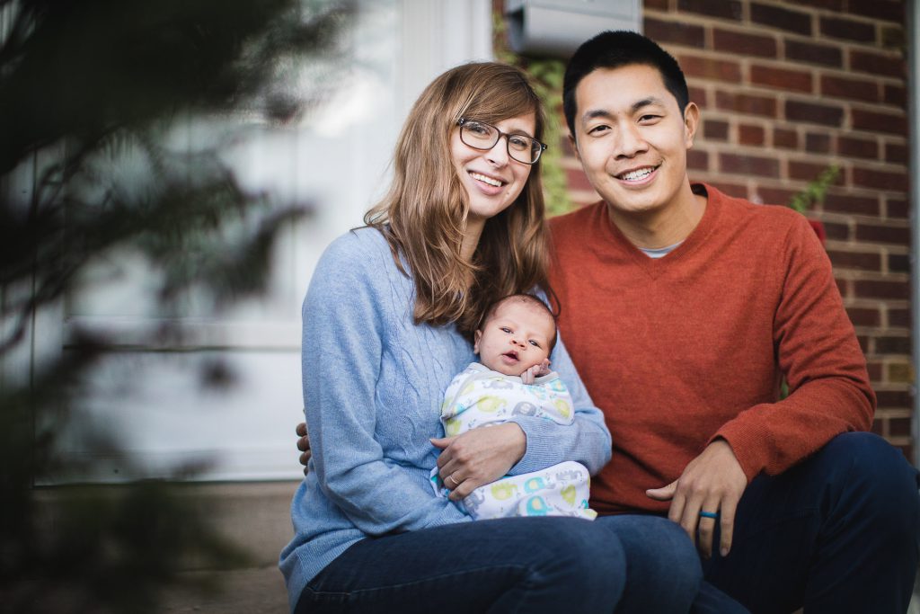 A family portrait with a man, woman, and baby in front of a house.