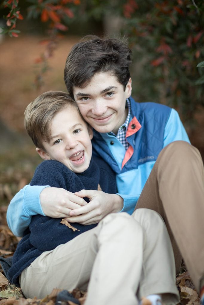 A boy and a girl sit together in the leaves for a family portrait.