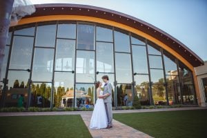 A wedding couple posing for a portrait in front of a large glass building.