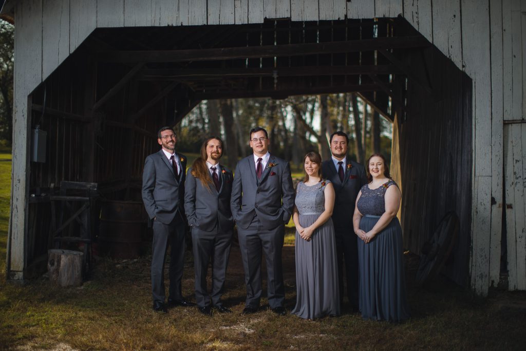 A group of groomsmen posing in front of a barn at a wedding.