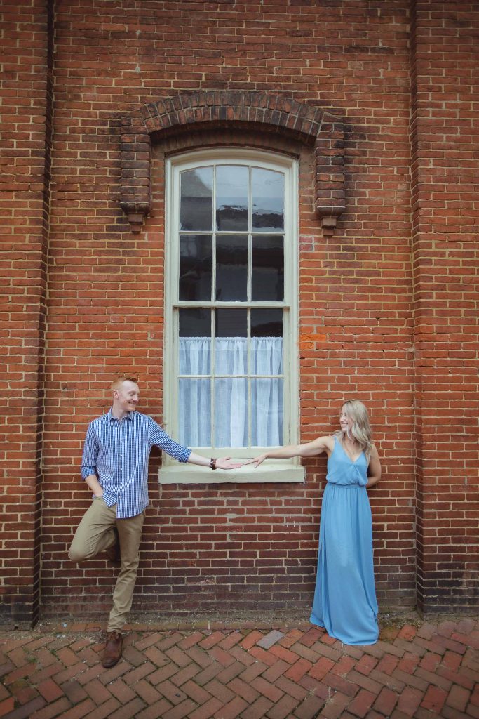 An engagement photo of a couple holding hands in front of a brick building in downtown Annapolis.