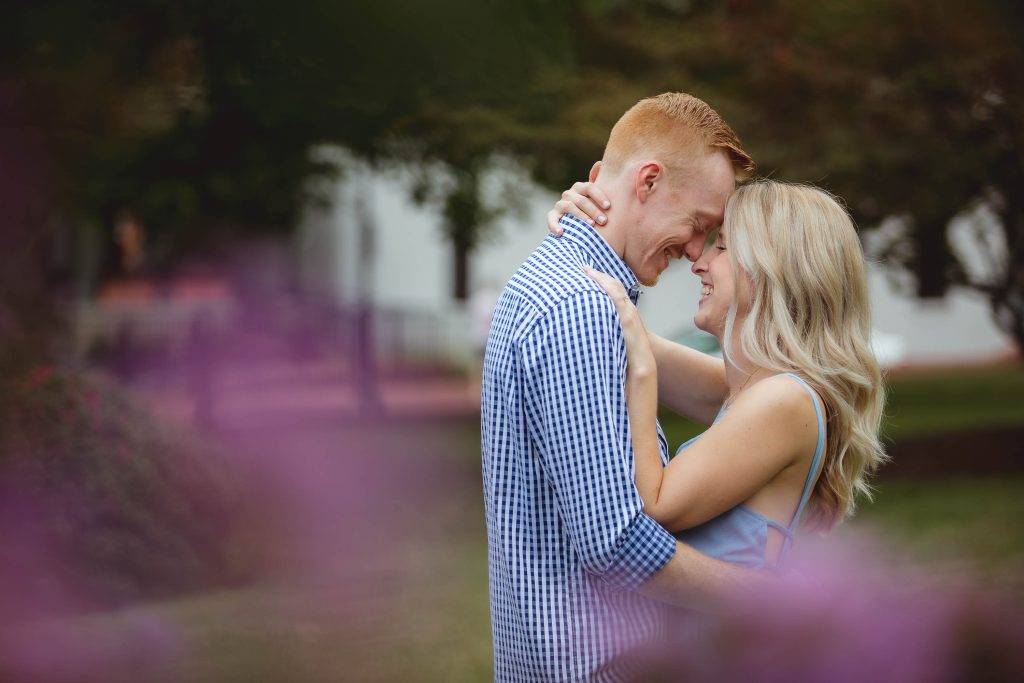 A couple embraces in front of purple flowers during their engagement session in Downtown Annapolis.