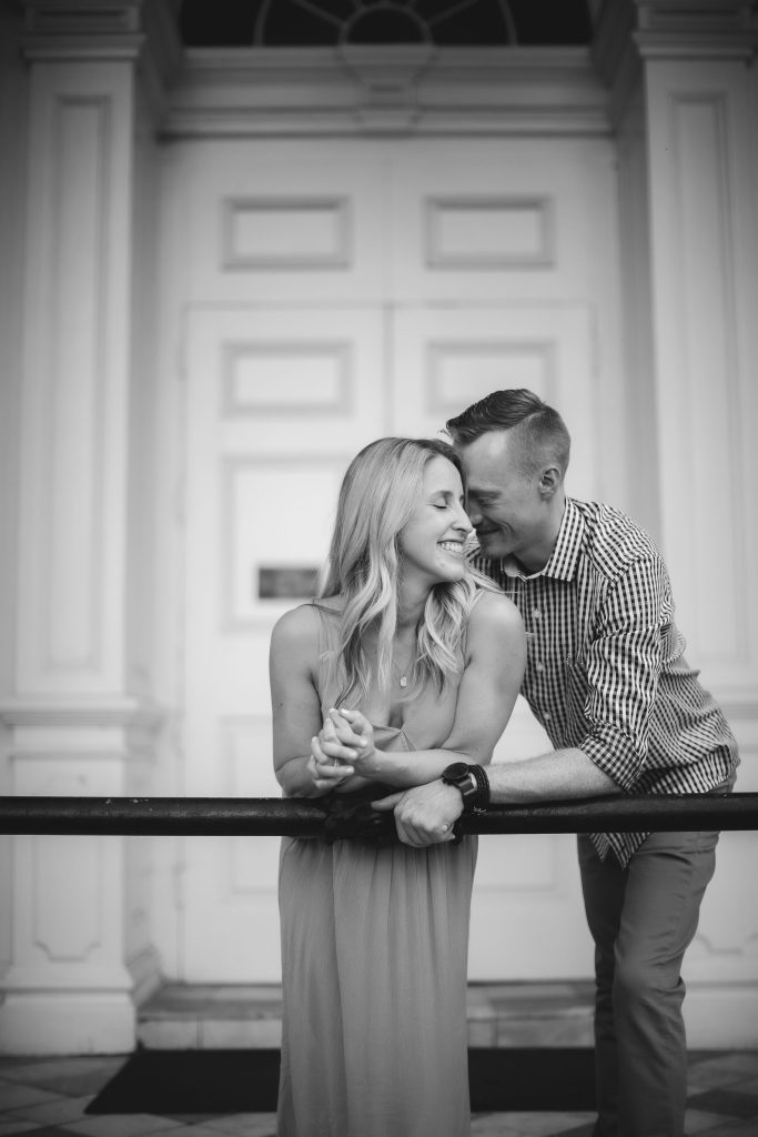 A black and white portrait of an engaged couple leaning against a railing in Downtown Annapolis.