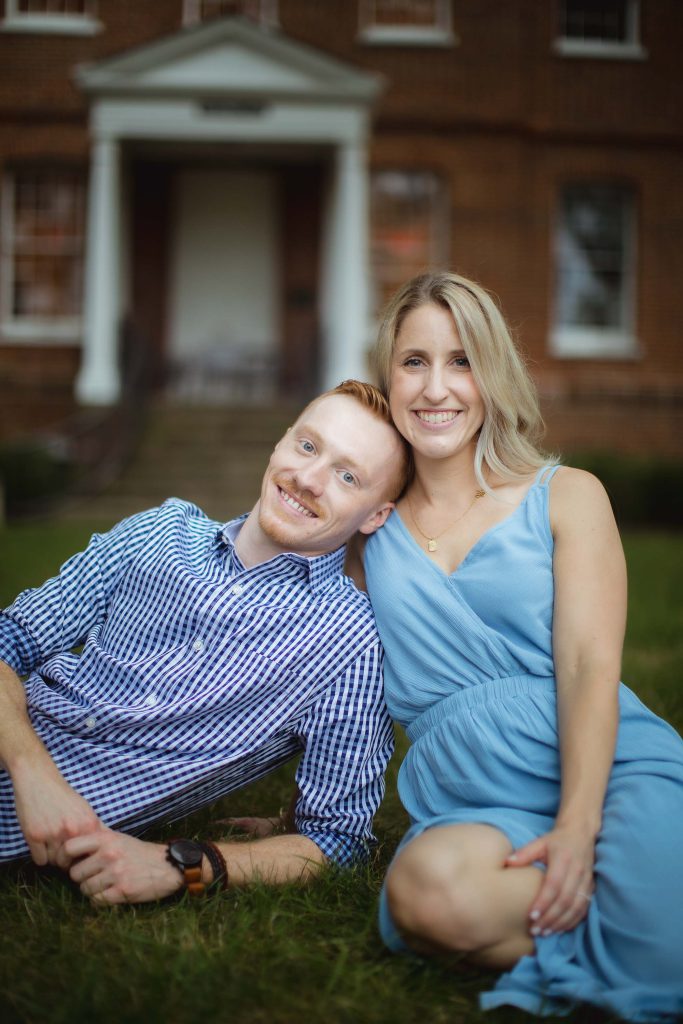 An engaged couple posing in front of a brick house for their engagement photo.