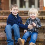 Two boys sitting on steps in front of a house during a family portrait session.