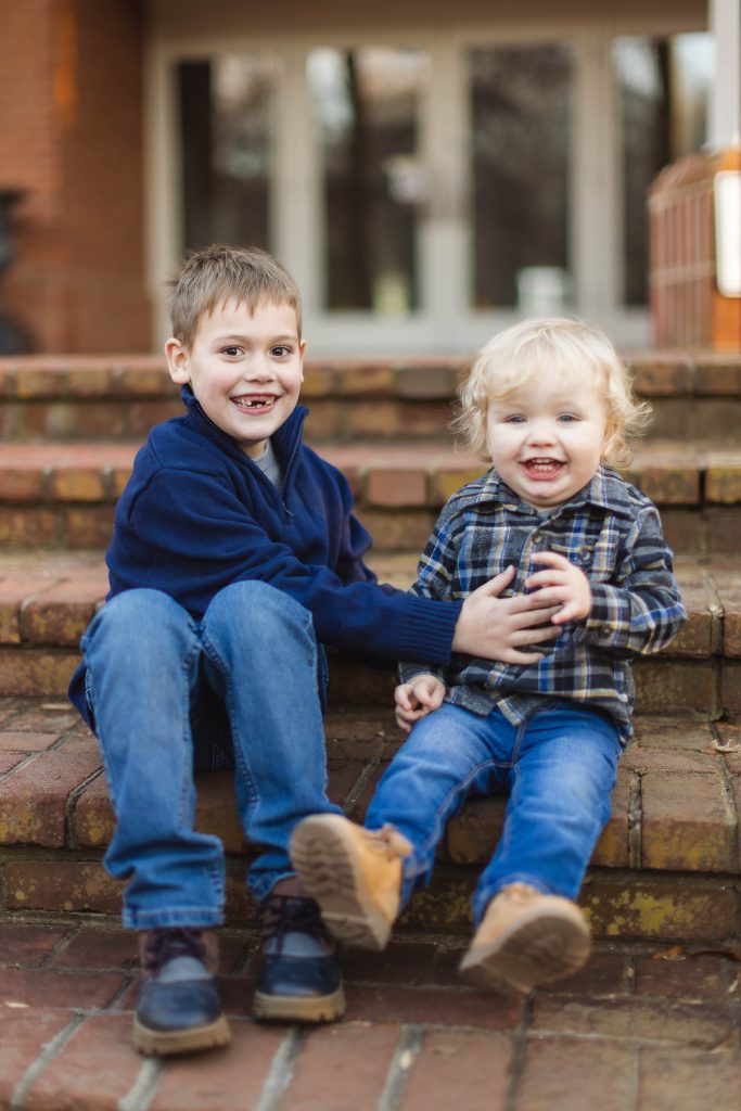 Two boys sitting on steps in front of a house during a family portrait session.