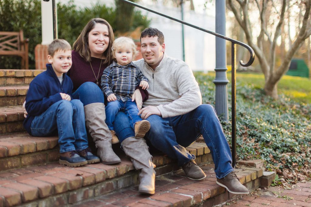 A family sits on the steps of their home, capturing beautiful portraits during their engagement session at Quiet Waters Park.