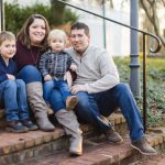 A family sits on the steps of their home, capturing beautiful portraits during their engagement session at Quiet Waters Park.