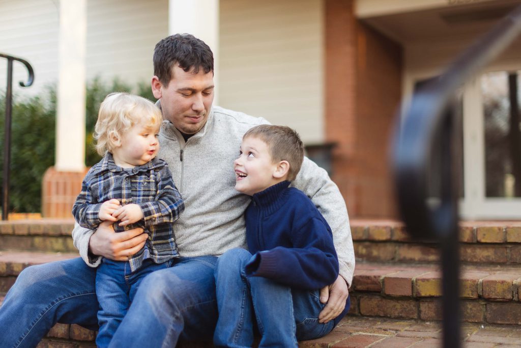 A man and two boys sitting on the steps of a house during a quiet engagement session.