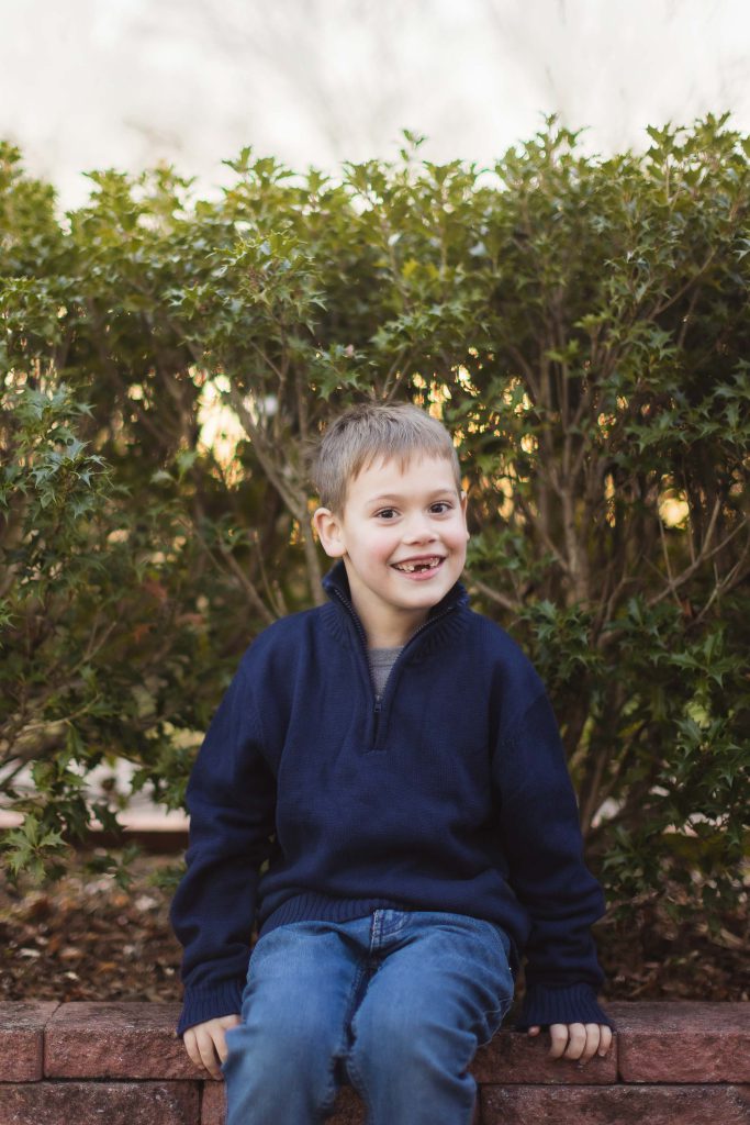 A young boy sitting on a brick wall in front of bushes at Quiet Waters Park.