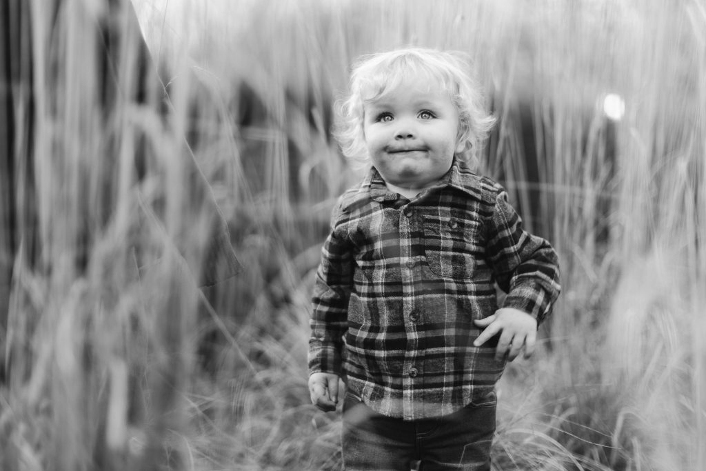 A black and white portrait of a little boy standing in tall grass at Quiet Waters Park.