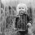 A black and white portrait of a little boy standing in tall grass at Quiet Waters Park.