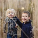 Two boys in tall grass smiling at each other during a family portraits session.