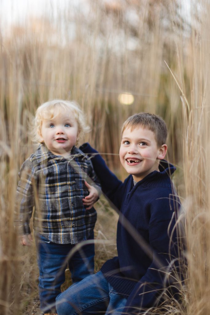 Two boys in tall grass smiling at each other during a family portraits session.