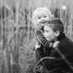 A monochrome portrait featuring a boy and a girl amidst tall grass during an engagement session.