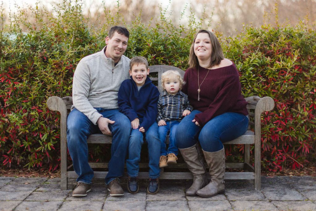 A family sits on a bench in front of bushes at Quiet Waters Park, capturing beautiful portraits.