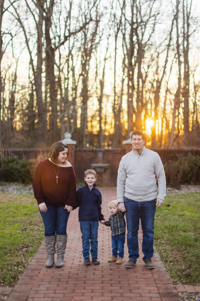A family is standing on a brick walkway during their engagement session at Quiet Waters Park at sunset.