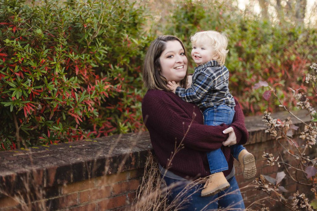 A family engaged in a portrait session, capturing the loving moment between a woman and her son against a brick wall.