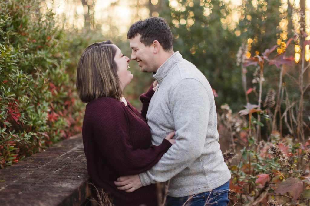 A couple embraces in front of a brick wall during their engagement session at Quiet Waters Park.