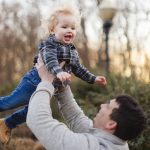 During a family photo session, a man joyfully holds his son in the air while capturing memorable portraits.