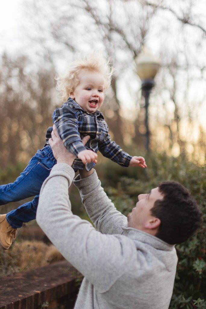 During a family photo session, a man joyfully holds his son in the air while capturing memorable portraits.