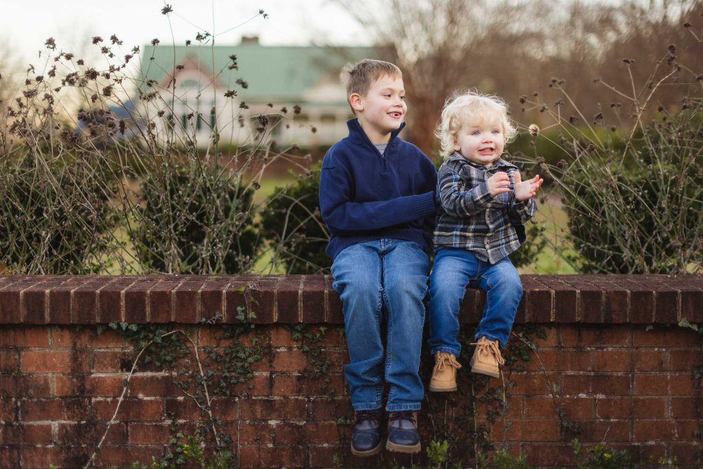 Two boys sitting on a brick wall in front of a brick wall during an engagement session at Quiet Waters Park.