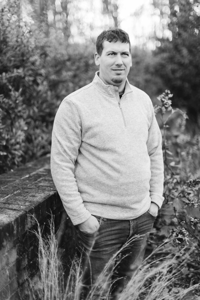 A black and white photo of a man leaning against a wall during an Engagement Session.