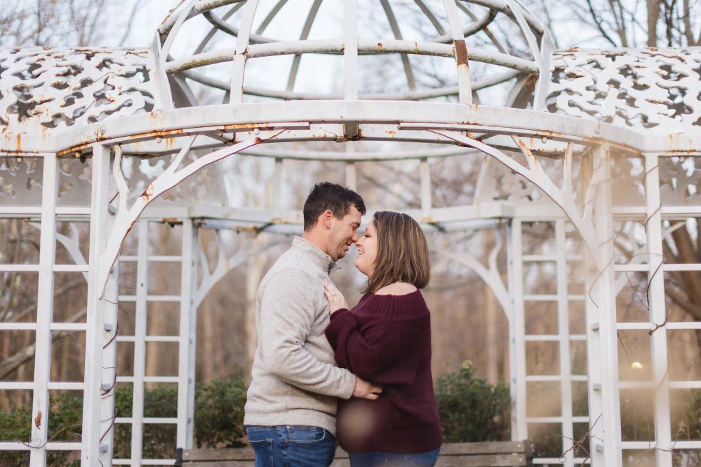 A couple embraces in front of an ornate gazebo during their engagement session.