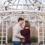 A couple embraces in front of an ornate gazebo during their engagement session.