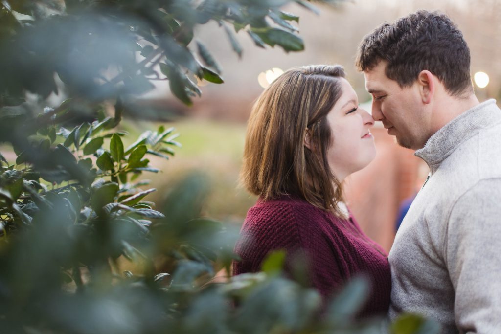A couple shares an intimate moment in front of lush bushes during their engagement session at Quiet Waters Park.