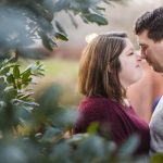 A couple shares an intimate moment in front of lush bushes during their engagement session at Quiet Waters Park.