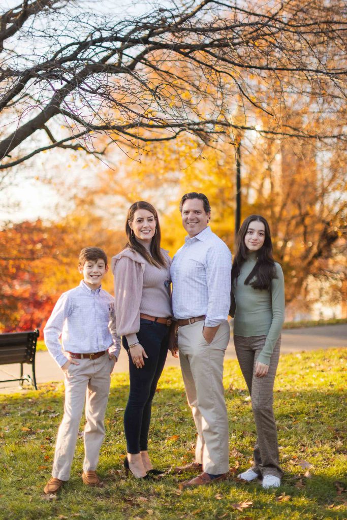 A Family is posing for portraits in front of a tree at Federal Hill Park.