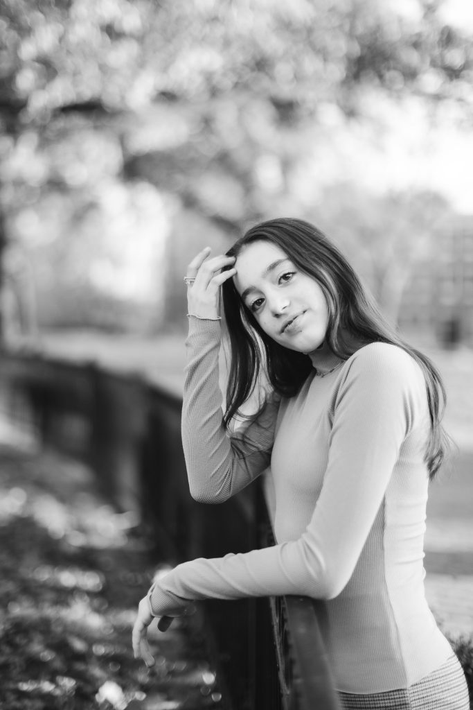 A black and white photo of a woman leaning against a fence.