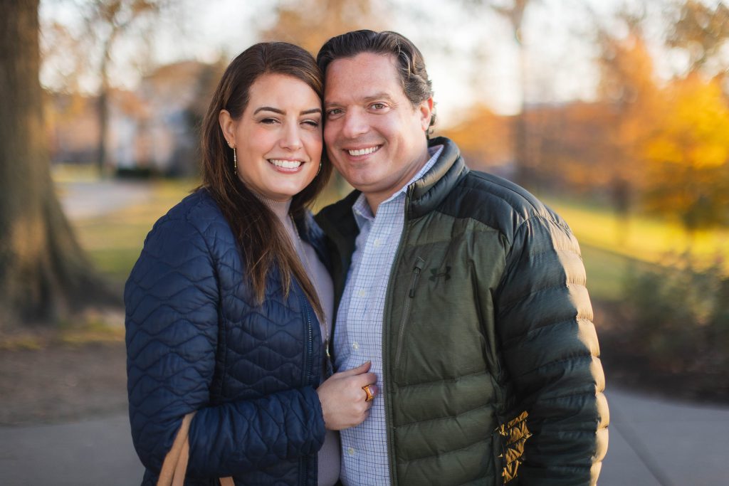 A man and woman are posing for their engagement session portraits at Federal Hill Park.