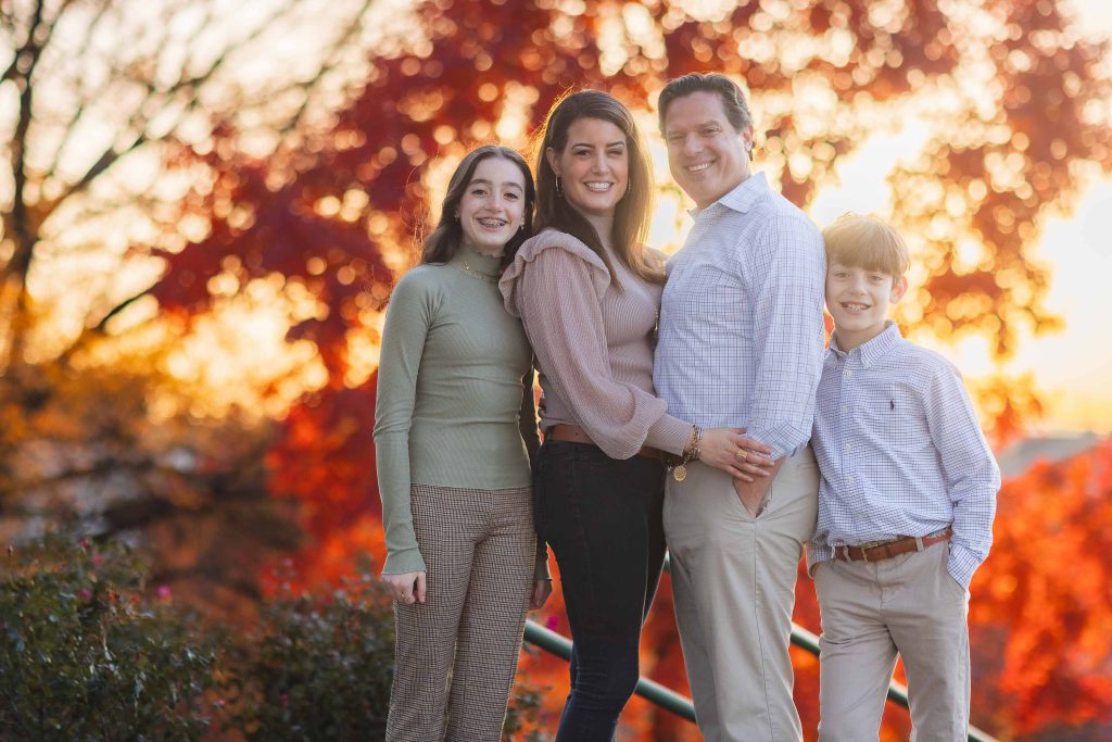 A family is posing for a portrait in front of an autumn tree.